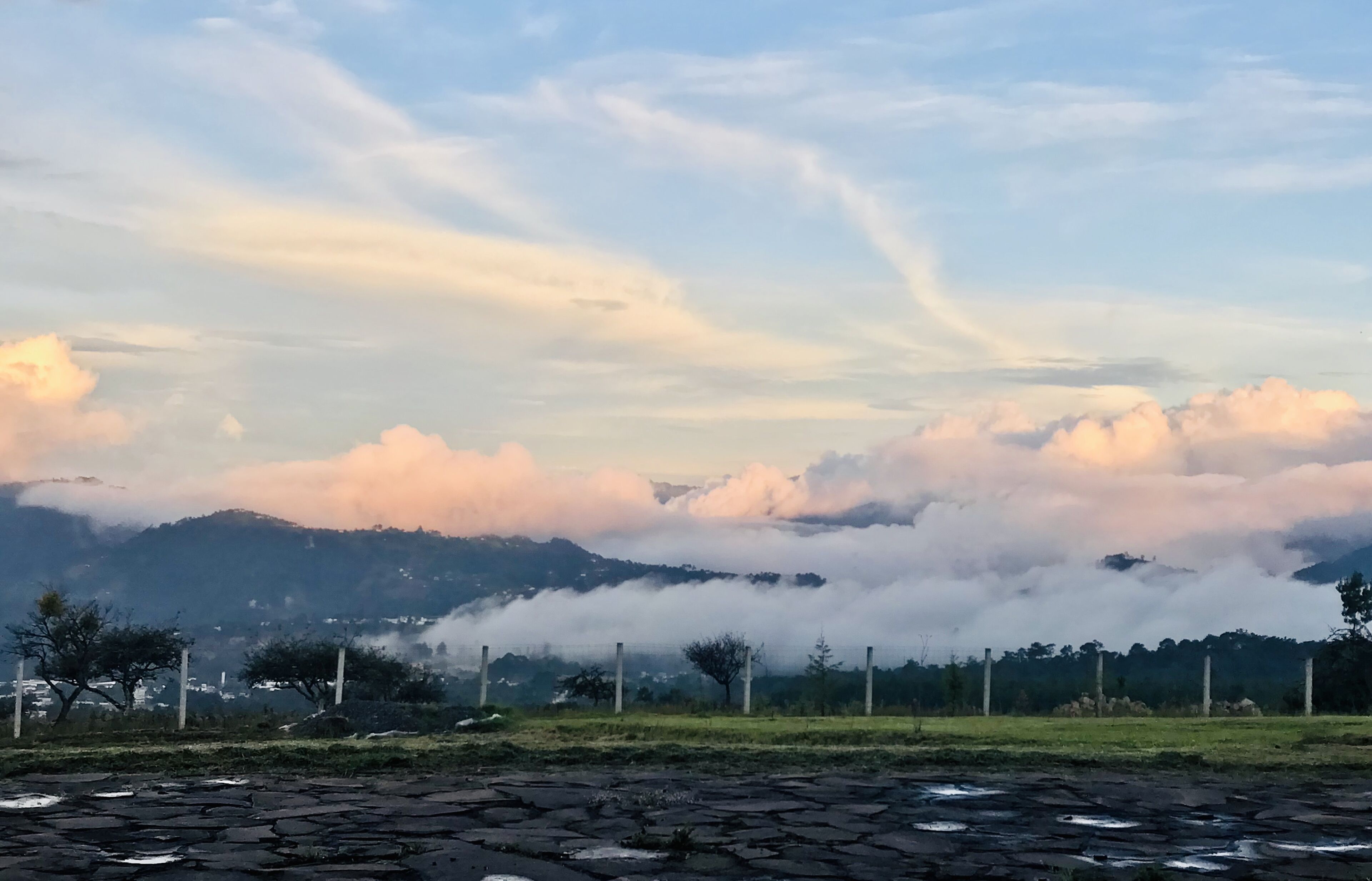 Un paisaje con una cadena montañosa, una cerca y una carretera.