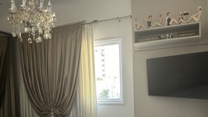 Ein Schlafzimmer mit einem großen Bett, einer Kristallleuchter, einem an der Wand montierten Fernseher und einem Fenster mit Vorhängen.