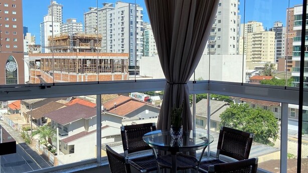 Ein Balkon mit einem Glastisch und vier Korbstühlen, mit Blick auf eine Stadtlandschaft mit Gebäuden und einer Baustelle.