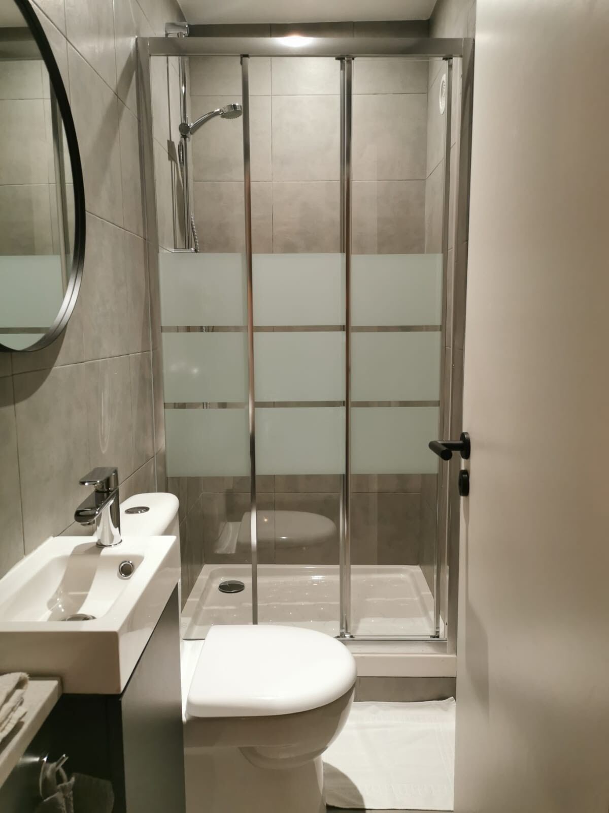 Ein modernes Badezimmer mit einer Duschkabine, einem weißen Waschbecken und einer Toilette.