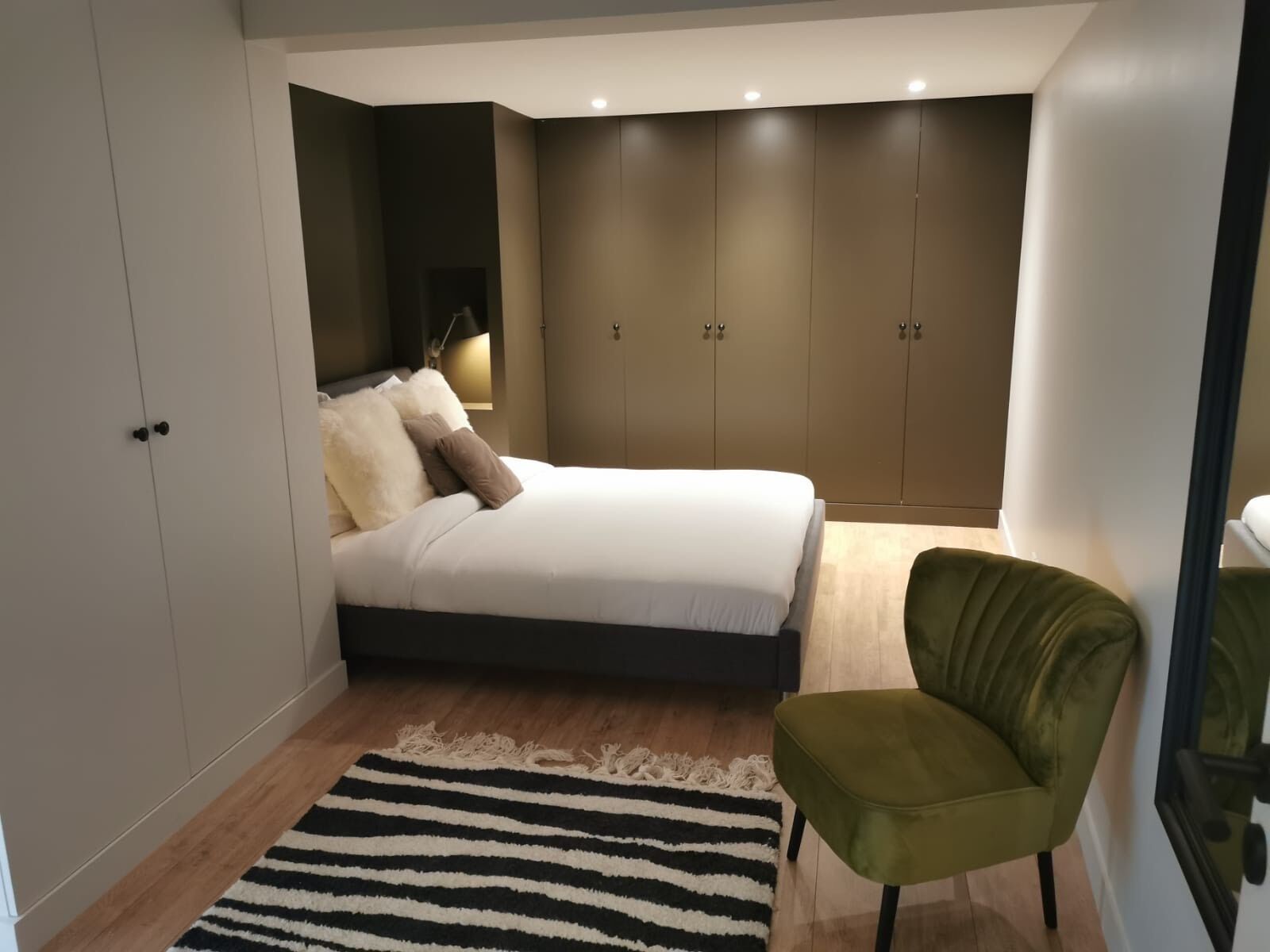 A bedroom with a bed, a green chair, a striped rug, and a wardrobe.