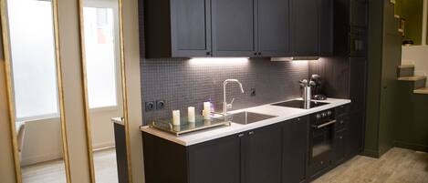 A modern kitchen with dark cabinetry, a white countertop, and a stainless steel sink.