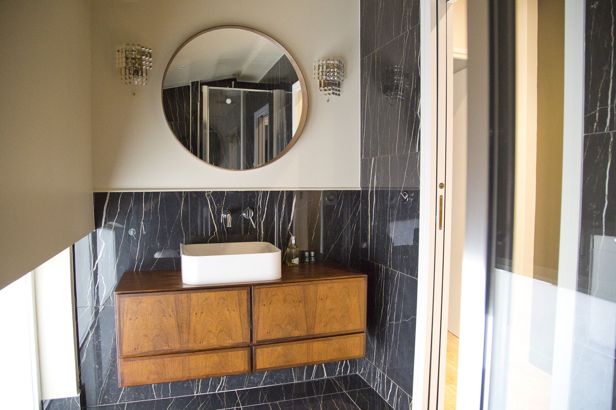 A bathroom with a round mirror, a white sink, and wooden cabinets.