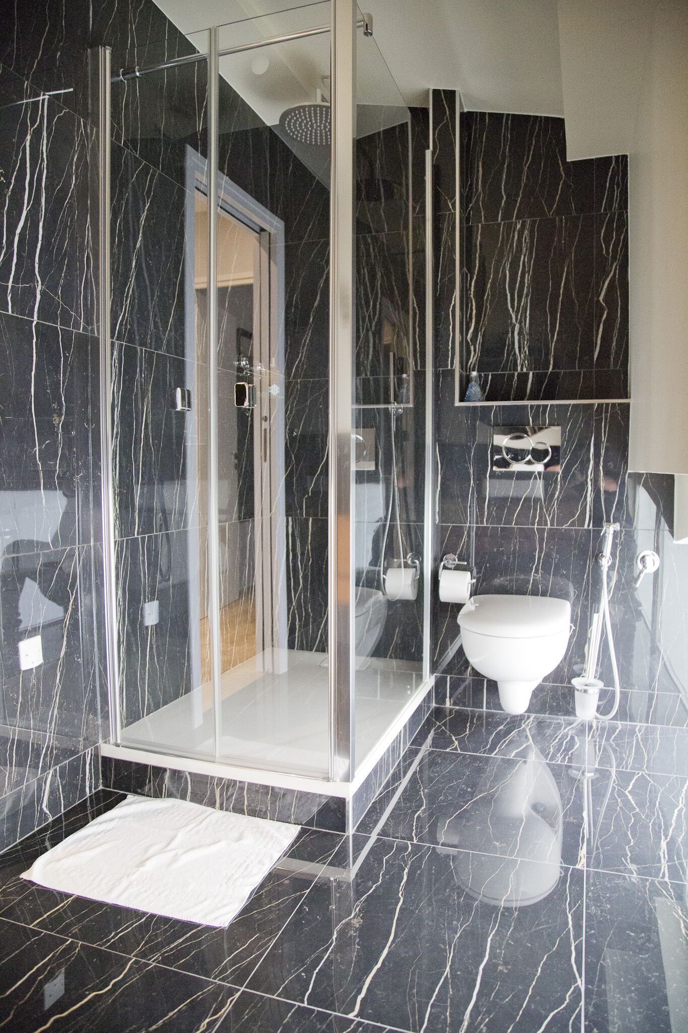 Un baño moderno con ducha de mampara de vidrio, inodoro blanco y suelo de mármol.
