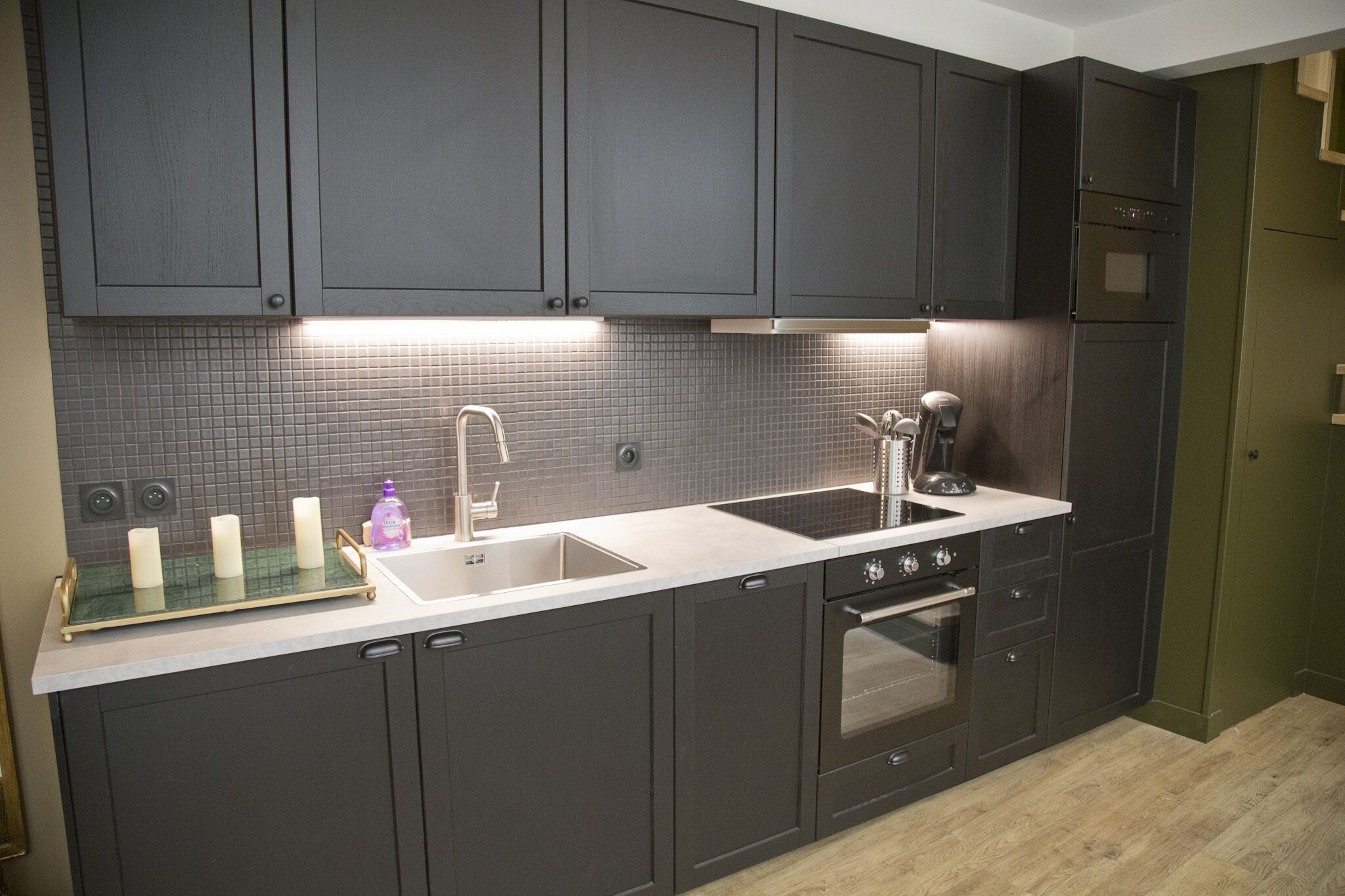 A modern kitchen with dark cabinets, a stainless steel sink, and a built-in oven.