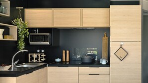 A modern kitchen with wooden cabinets, a black countertop, a microwave, a sink, and a hanging plant.