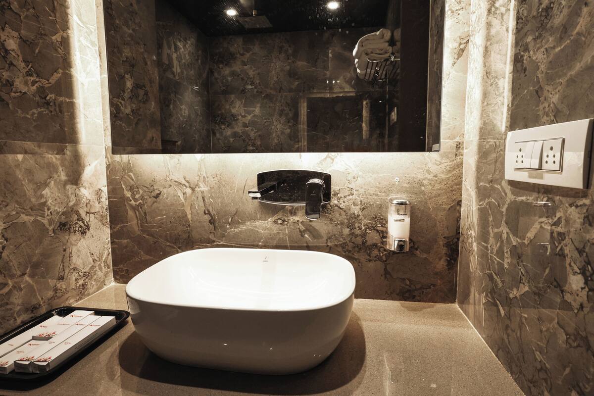 Un baño con un lavamanos blanco grande y ovalado, un espejo encima y una pared de mármol.
