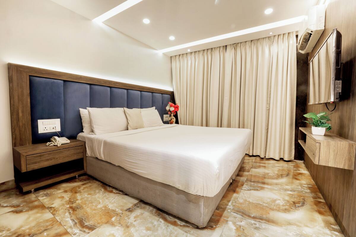 Habitación de hotel moderna con una cama grande, mesita de noche de madera y televisión integrada.