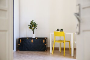 Une pièce avec une table blanche, une chaise jaune et un coffre noir sur lequel est posée une plante en pot.