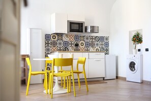 Une cuisine compacte équipée d’un four à micro-ondes, d’un lave-linge et d’un coin repas avec des chaises jaunes.
