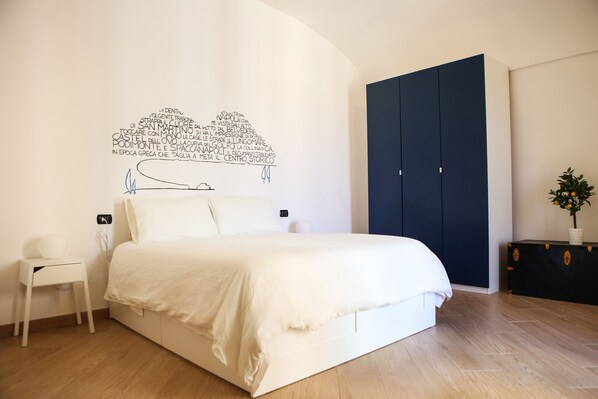 A bedroom with a bed, a nightstand, a dresser, and a dark blue wardrobe.