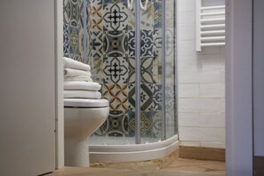 A bathroom with a white toilet, a glass shower enclosure, and patterned tiles on the walls.