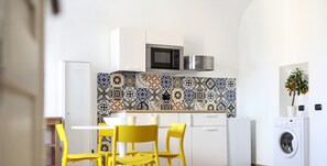 A modern kitchen with a microwave, a washing machine, and a dining area with yellow chairs.