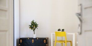 A room with a white table and a yellow chair, a black suitcase with a plant, and a small potted plant on the table.