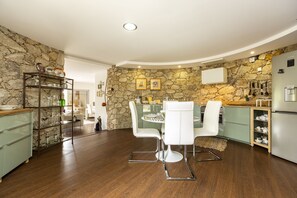 Una cocina moderna con pared de piedra, suelo de madera, sillas blancas y un refrigerador empotrado.