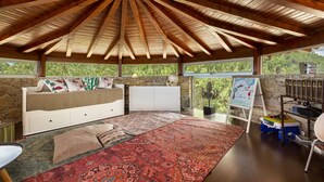 Une chambre avec un plafond en bois, un lit agrémenté de coussins décoratifs, une grande moquette et une vue sur la verdure à l’extérieur.