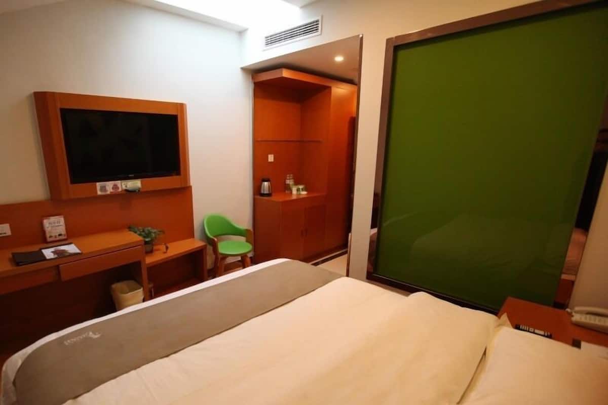 Ein Hotelzimmer mit einem Bett, einem Schreibtisch mit Stuhl, einem Fernseher und einer grünen Schiebetür.