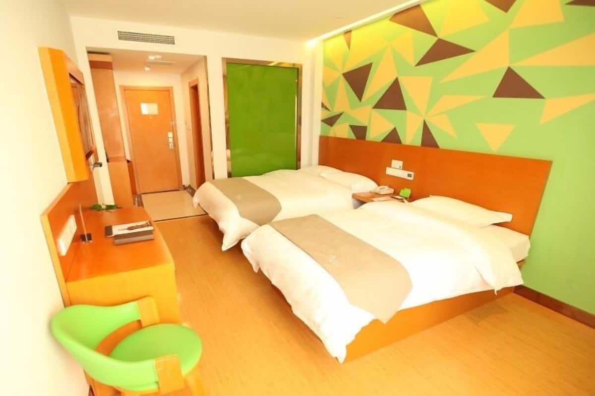 Ein Hotelzimmer mit zwei Betten, einem Schreibtisch, einem Stuhl und einer grünen Wand mit geometrischen Mustern.