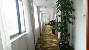 A hotel hallway with patterned flooring, large windows, and potted plants. - Vatica Qingdao Licang Xiazhuang Hexie Plaza Hotel (Qingdao)