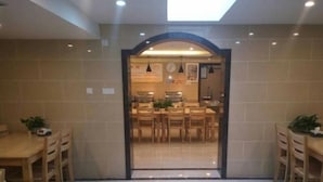A dining area with a high ceiling, tiled walls, and a skylight. There are wooden tables and chairs, and a kitchen area is visible through an archway. - Vatica Qingdao Licang Xiazhuang Hexie Plaza Hotel (Qingdao)
