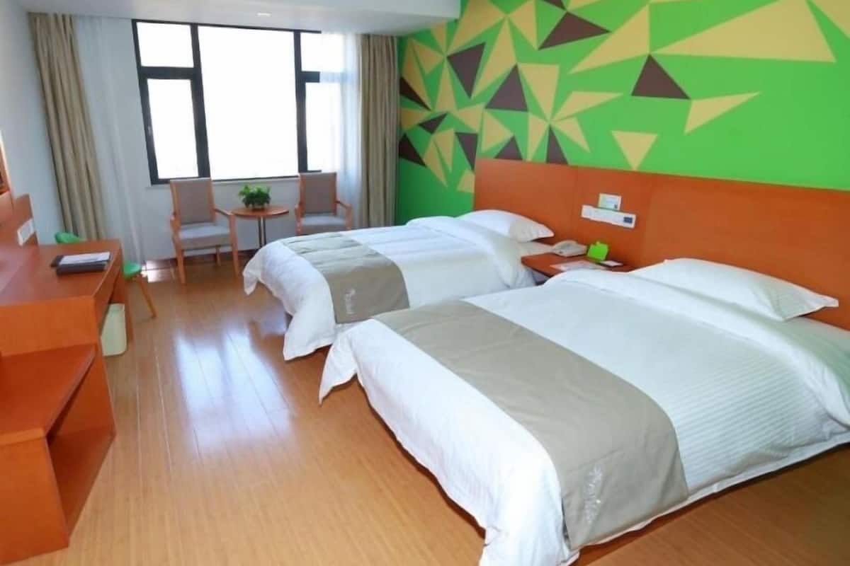 Ein Hotelzimmer mit zwei Betten, einem Schreibtisch, einem Stuhl und einem Fenster.