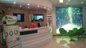A reception area with a curved counter, two receptionists, a digital screen, and a large wall mural. - Vatica Qingdao Licang Xiazhuang Hexie Plaza Hotel (Qingdao)