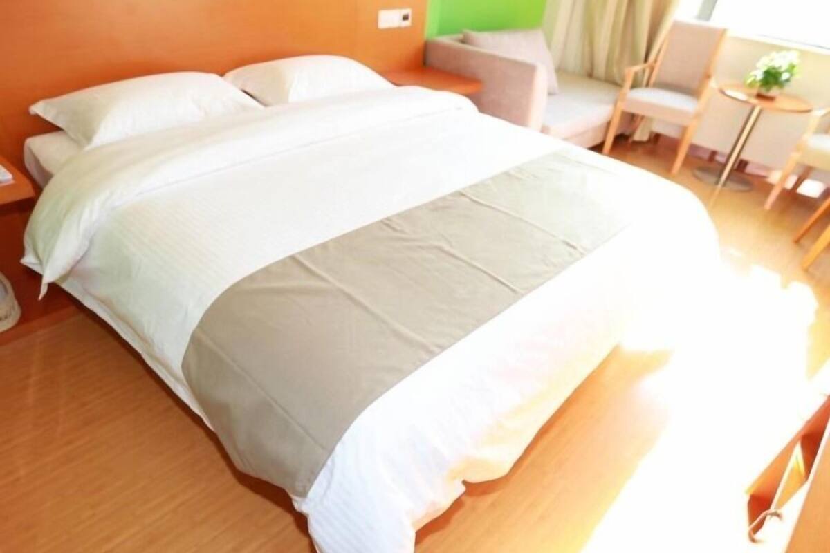 Ein ordentlich bezogenes Bett mit weißen Leinen in einem Zimmer mit orangefarbenen Wänden und einer Wand in Grüntönen.