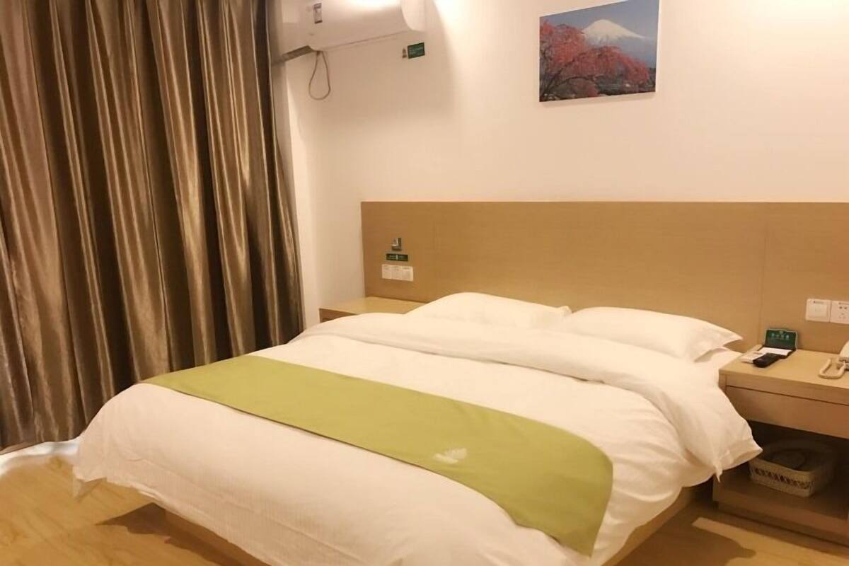 A hotel room with a bed, a nightstand, a telephone, and a painting of a mountain.