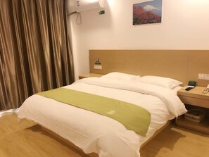 Una habitación de hotel con una cama, una mesita de noche, un teléfono y un cuadro de una montaña.