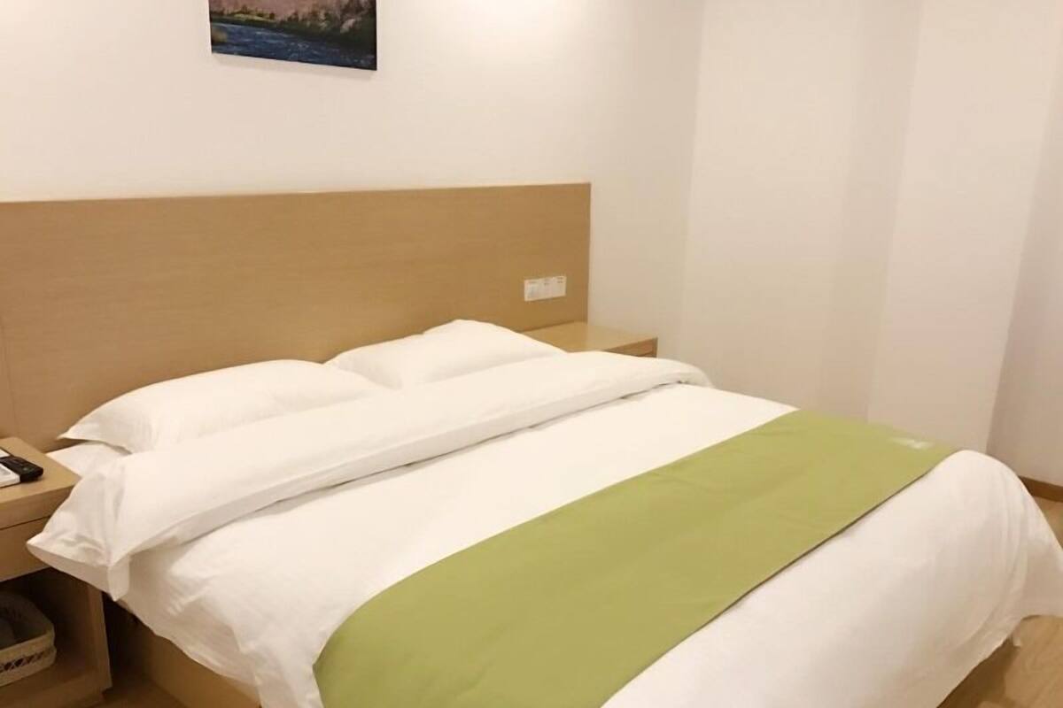 A neatly made bed with white and green bedding, a wooden headboard, and a small bedside table with a lamp.