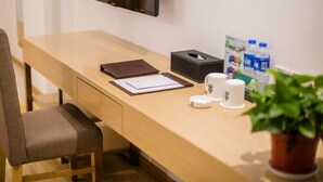 Un escritorio moderno con una silla, un televisor de pantalla plana montado en la pared, una caja de pañuelos, una botella de agua, una taza y una planta en maceta.