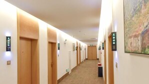 Un pasillo de hotel con puertas de madera, pisos alfombrados y letreros iluminados que muestran los números de las habitaciones.