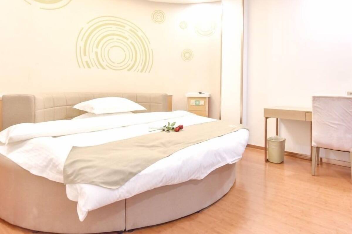 Una habitación de hotel moderna con una cama redonda, una mesita de noche, un escritorio y un cesto de basura.