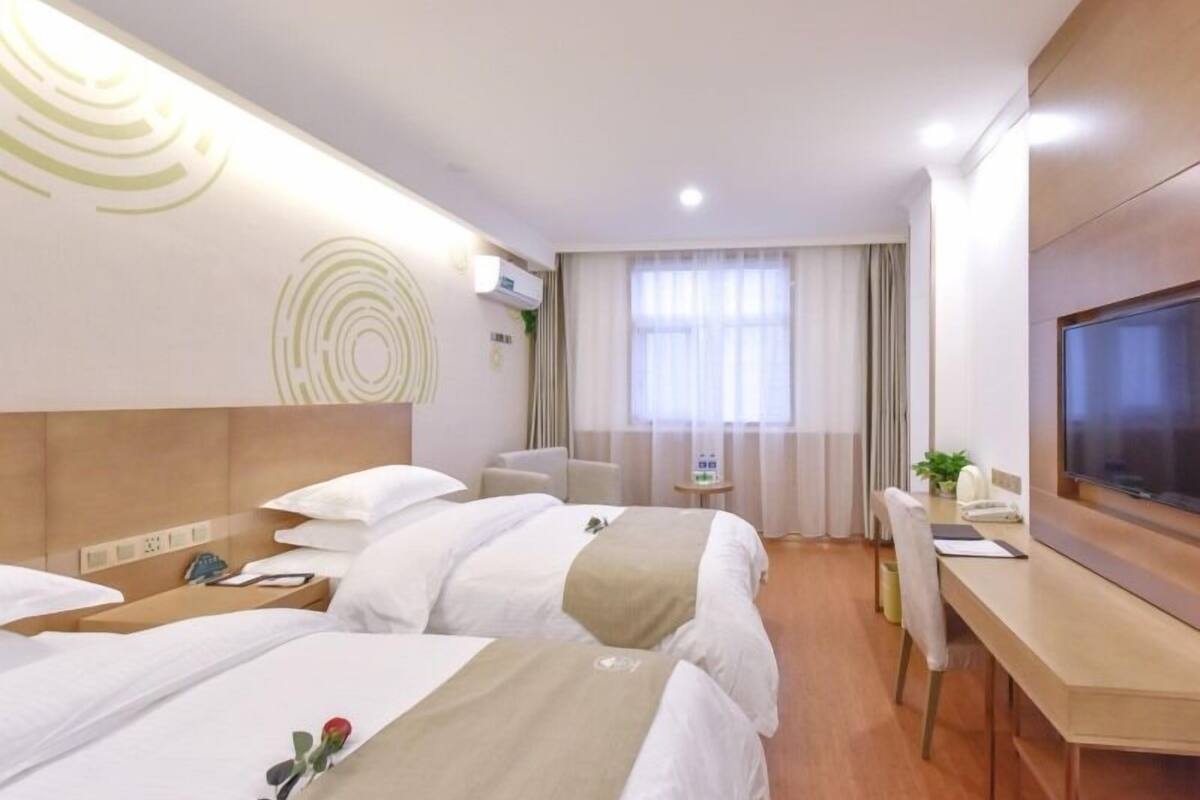 Una habitación de hotel con dos camas, un escritorio, un televisor y una ventana con cortinas.