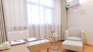 Habitación de hotel con un escritorio de madera, un sillón cómodo, una mesita redonda con botellas de agua y un teléfono.