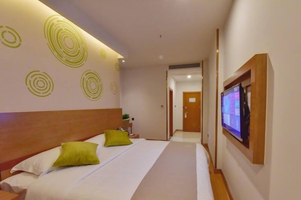 Habitación de hotel con cama, dos almohadas, televisor en la pared y puerta que da a otra habitación.