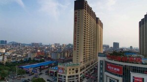 Un immeuble de grande hauteur à la façade structurée en forme de grille, entouré d’une zone commerciale comprenant divers magasins et bordé par une rue animée.