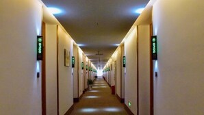 Un long couloir étroit, typique des hôtels, avec des portes des deux côtés, chacune portant un numéro.