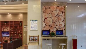 Un hall d’entrée avec un mur en rondins de bois, un comptoir d’accueil, deux tabourets de bar, un canapé et un écran de télévision.