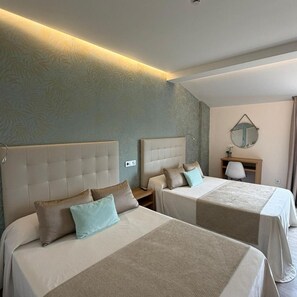 A hotel room with two beds, a desk, a chair, a mirror, and a wall-mounted light fixture.