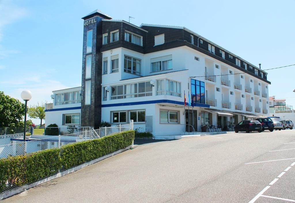 Um hotel de vários andares com um letreiro chamativo 'HOTEL', uma varanda no segundo andar e um estacionamento à frente.