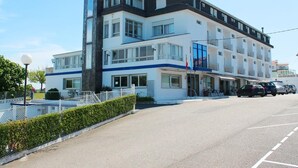A multi-story hotel with a prominent 'HOTEL' sign on the facade, a parking lot in front, and a flagpole with flags. - Marola (Sanxenxo)
