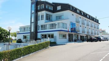 Um hotel de vários andares com um letreiro chamativo 'HOTEL', uma varanda no segundo andar e um estacionamento à frente.