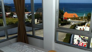 A bedroom with a bed, a window with a view of the sea, and a hat on the bed. - Marola (Sanxenxo)
