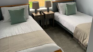 Een slaapkamer met twee eenpersoonsbedden, een raam met uitzicht op een tuin en een bureau met twee lampen.