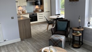 Een moderne keuken met een centraal kookeiland, een eethoek met een ronde tafel, en een zithoek met een bank en stoelen.