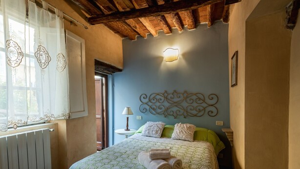 A bedroom with a bed, a nightstand, a lamp, and a decorative headboard. - Apartment Corte Fiorita Historical Center (Lucca)