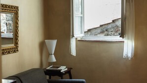 A room with a window, a lamp, a chair, and a table with books. - Apartment Corte Fiorita Historical Center (Lucca)