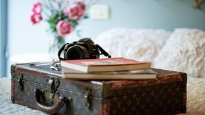 A vintage suitcase with a camera and books on a bed. - Apartment Corte Fiorita Historical Center (Lucca)