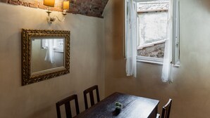 A dining area with a wooden table, four chairs, a mirror with a gold frame, and a wall-mounted light fixture. - Apartment Corte Fiorita Historical Center (Lucca)